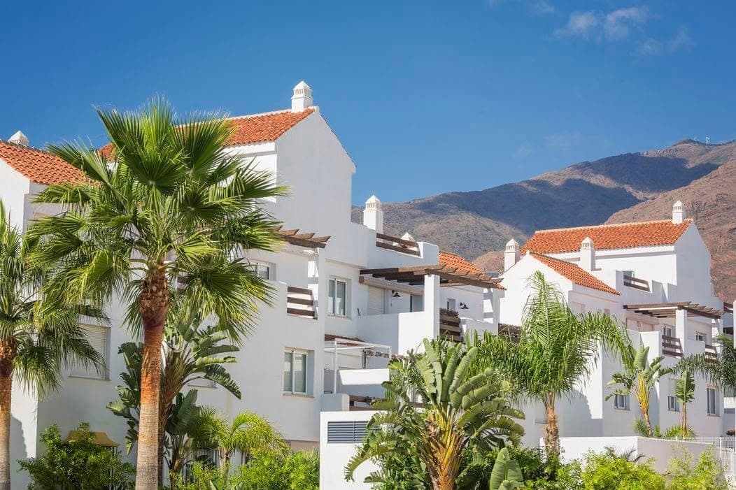 White apartment buildings among palm trees with mountains behind